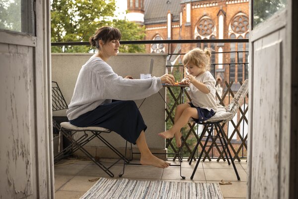 Mutter sitzt mit Kind bei Tisch auf dem Balkon